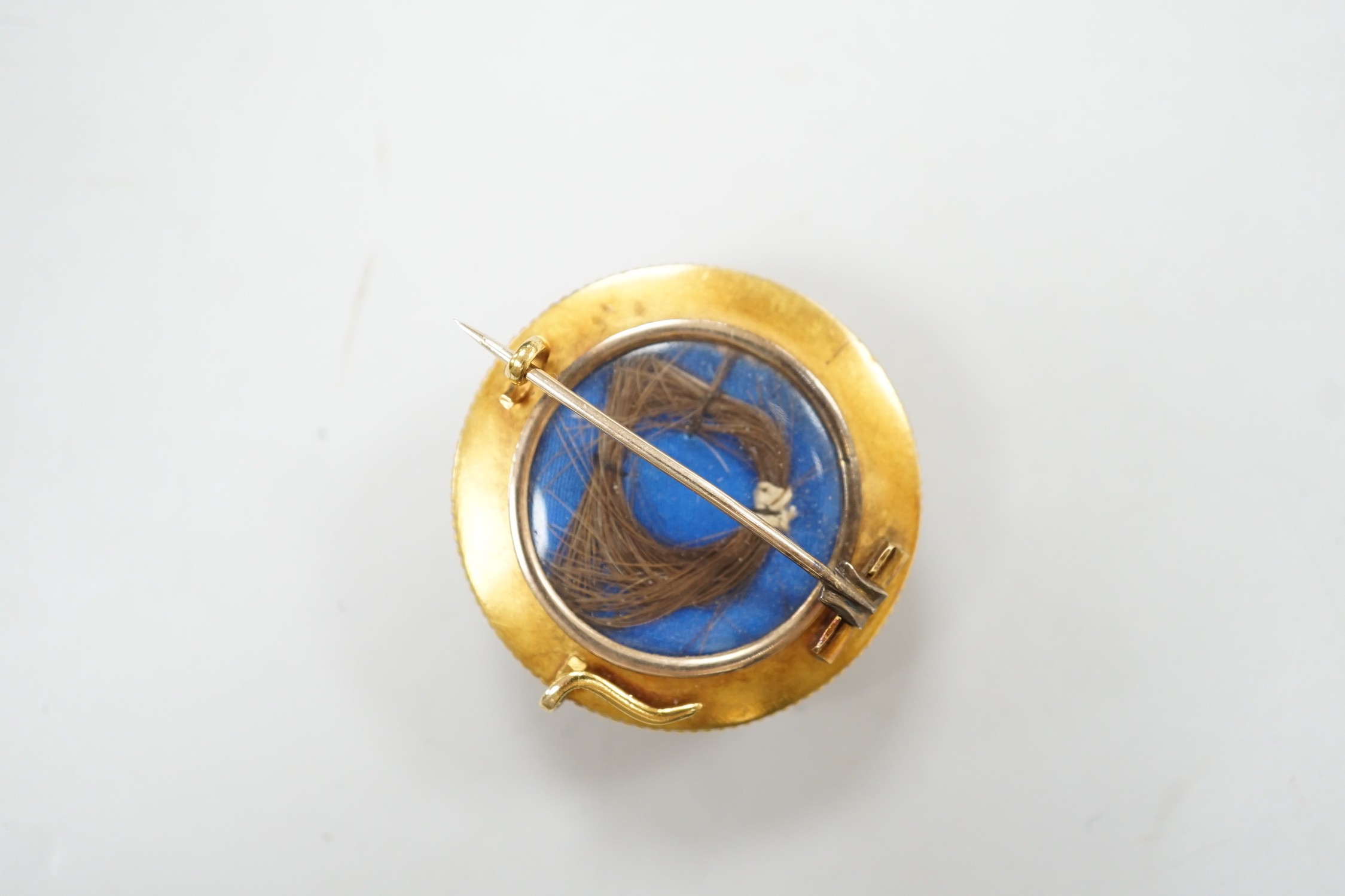 A cased Victorian yellow metal, enamel and split pearl set circular mourning pendant brooch, the glazed back with lock of hair beneath, diameter 34mm, gross weight 12.6 grams.